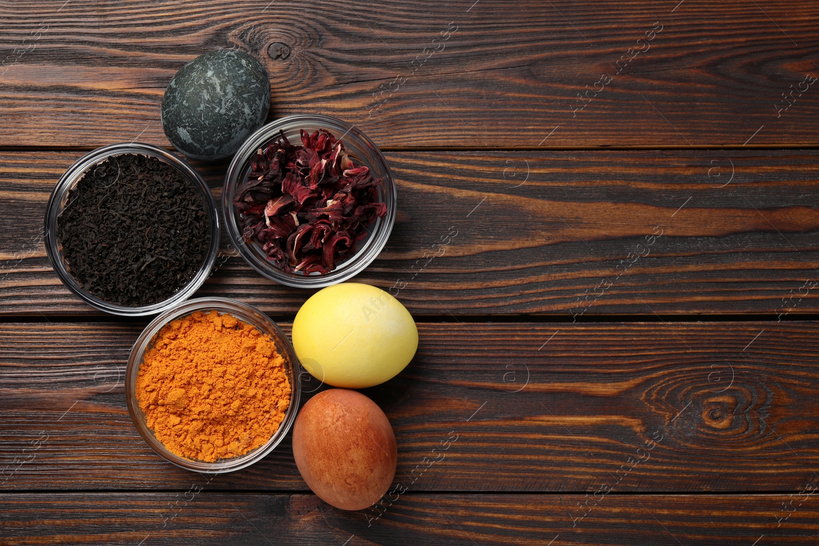 Photo of Painted Easter eggs with natural organic dyes (hibiscus, turmeric and tea) on wooden table, flat lay. Space for text