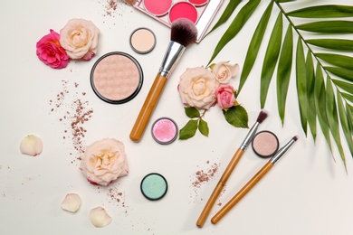 Photo of Flat lay composition with makeup brushes, cosmetic products and flowers on white background