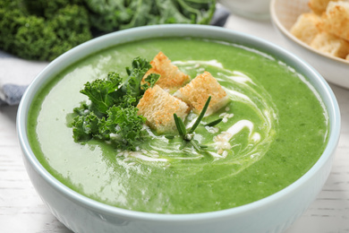 Tasty kale soup on white wooden table, closeup