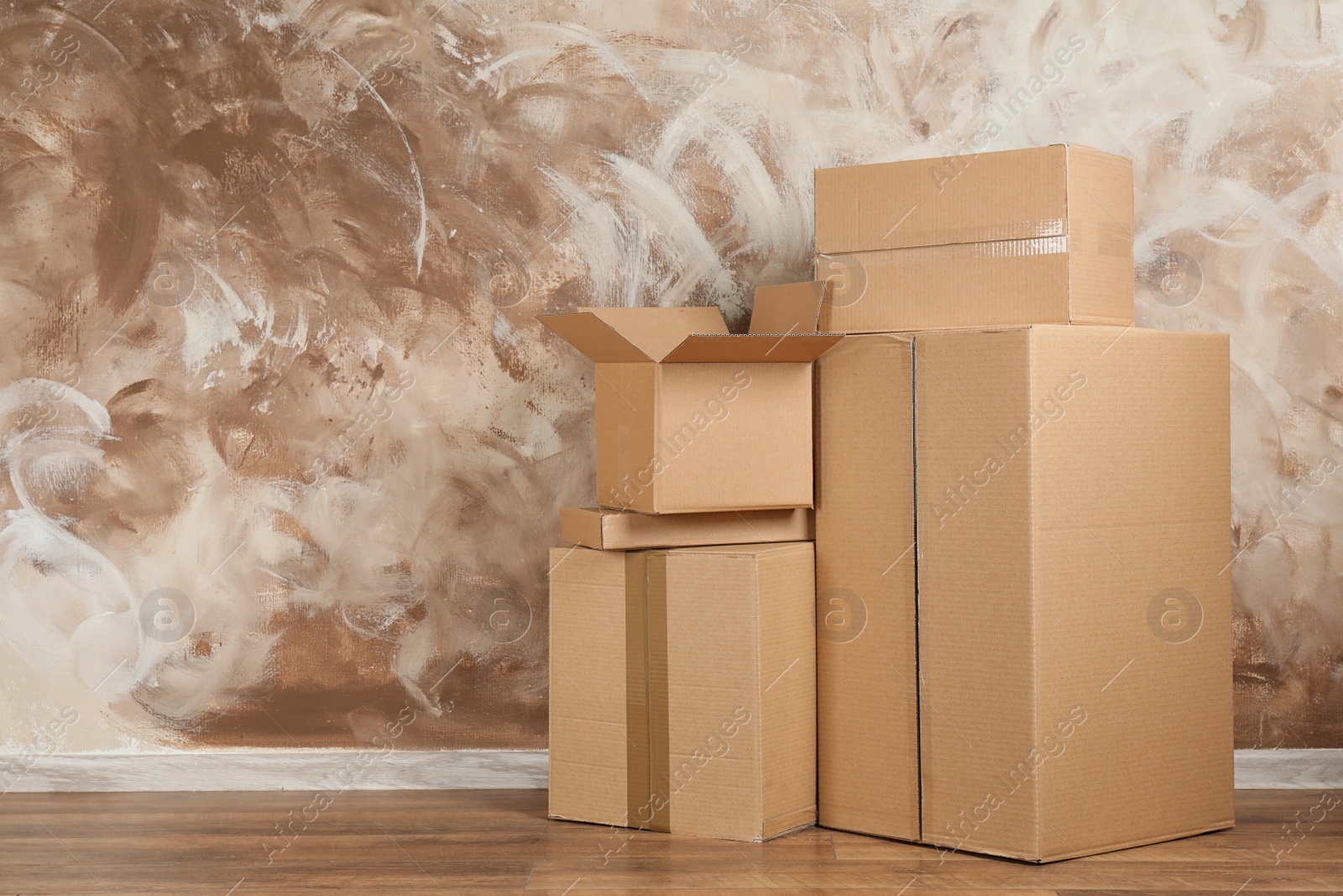 Photo of Pile of cardboard boxes near brown wall indoors. Space for text