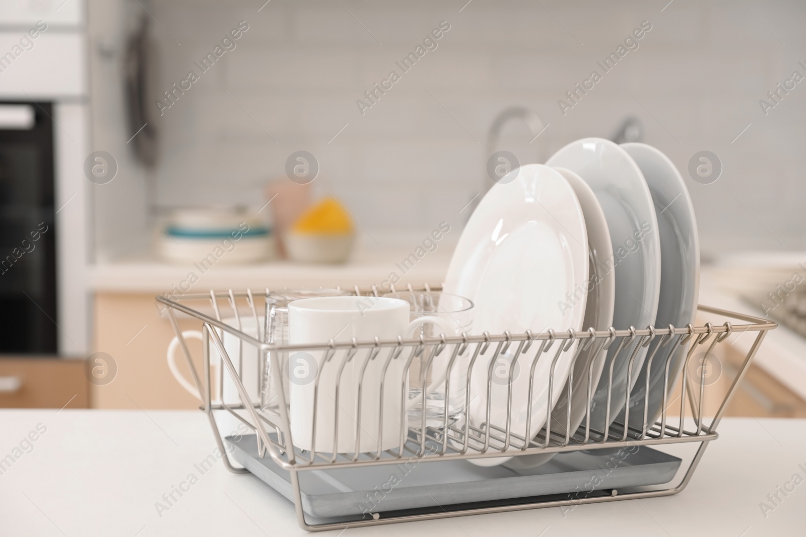 Photo of Dish drainer with clean dinnerware on table in kitchen