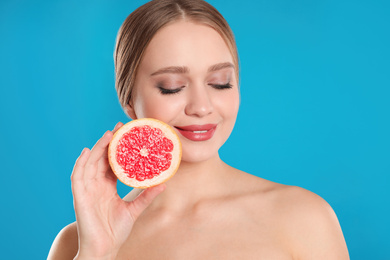 Photo of Young woman with cut grapefruit on blue background. Vitamin rich food