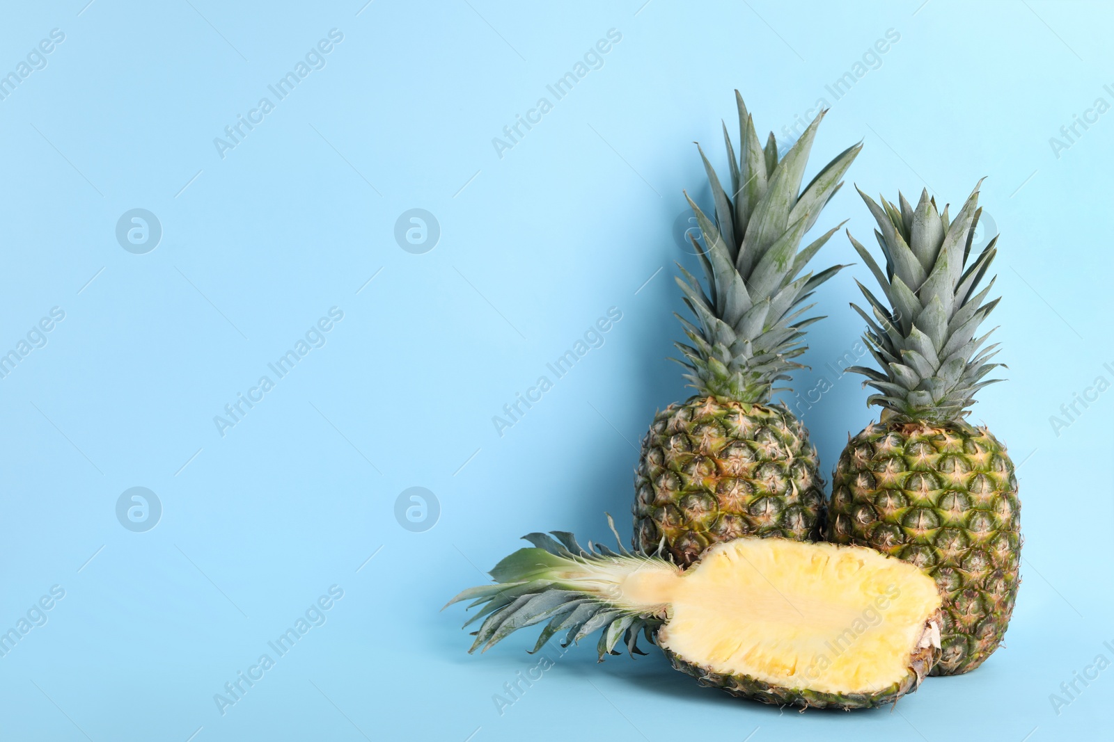 Photo of Whole and cut ripe pineapples on light blue background, space for text