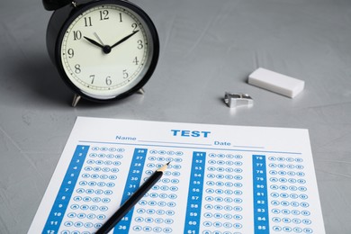 Photo of Answer sheet, pencil and alarm clock on light grey table. Student passing exam
