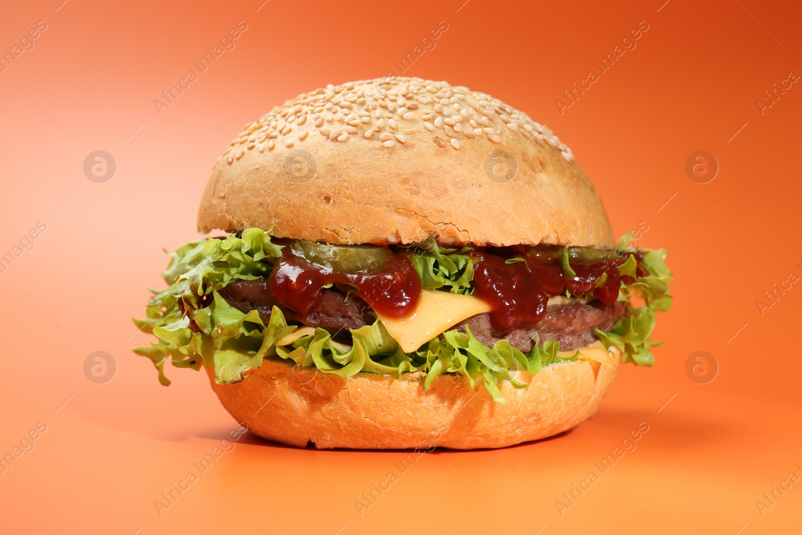 Photo of Delicious cheeseburger with lettuce, pickle, ketchup and patty on coral background, closeup