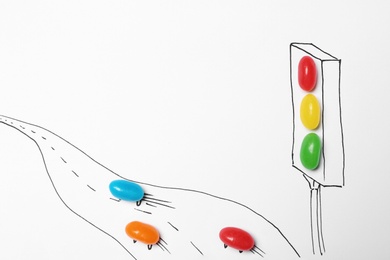 Photo of Colorful jelly candies arranged as traffic light and road with cars on white background, top view