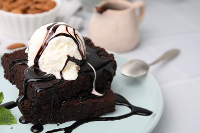 Photo of Tasty brownies served with ice cream and chocolate sauce on white table, closeup. Space for text