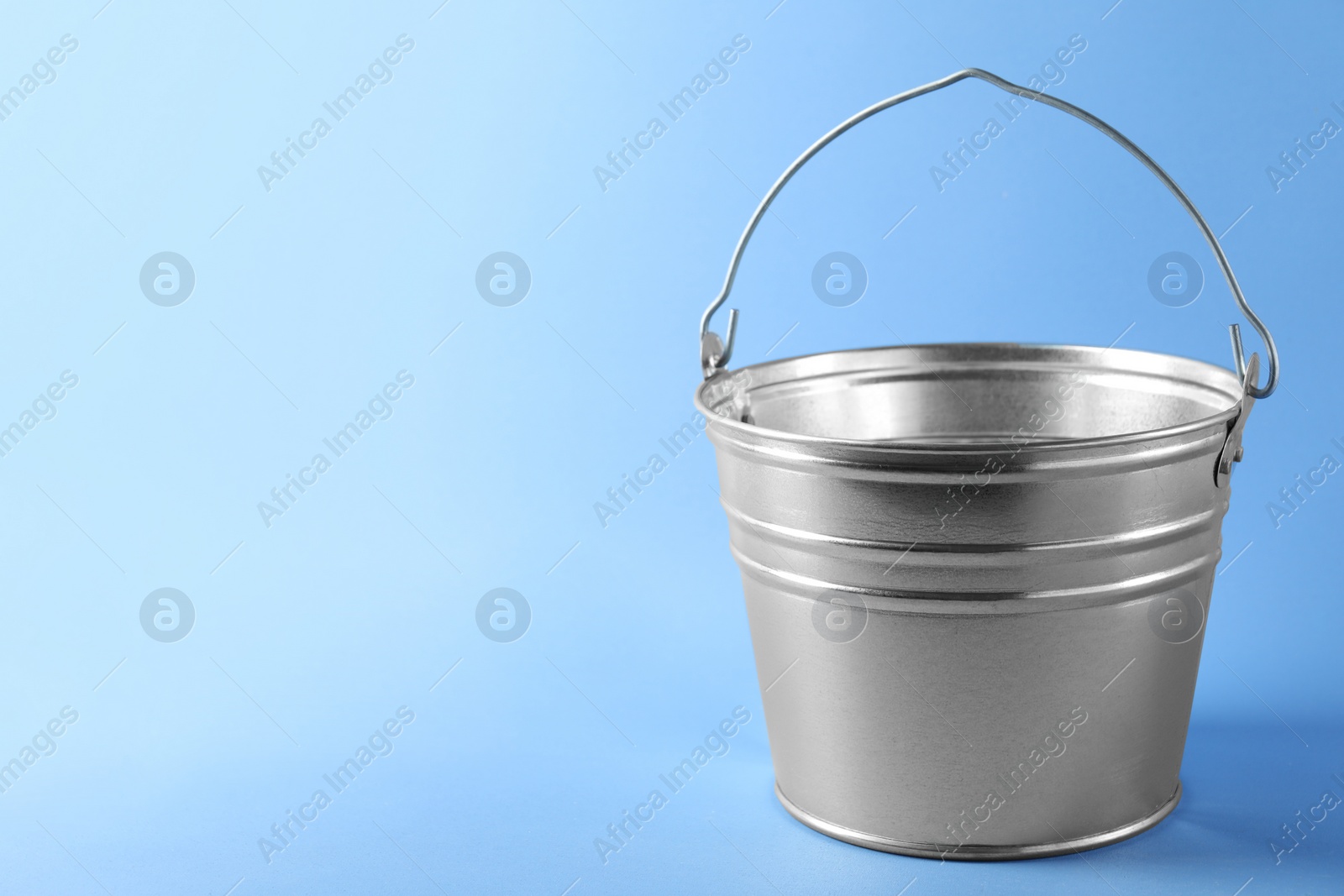 Photo of One shiny metal bucket on light blue background. Space for text