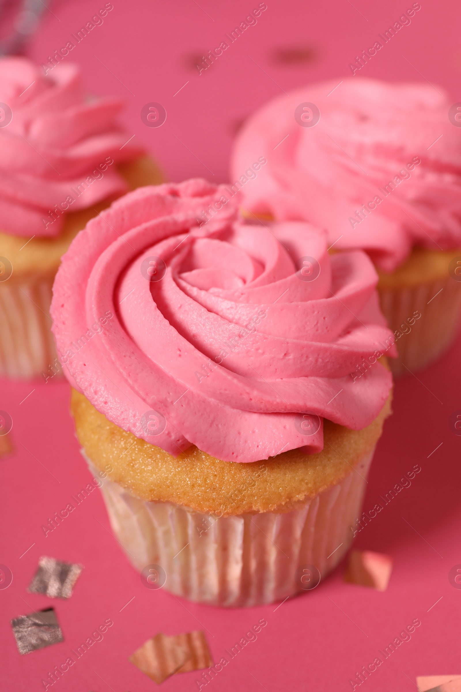 Photo of Delicious cupcakes with bright cream and confetti on pink background, closeup