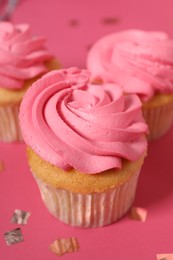 Delicious cupcakes with bright cream and confetti on pink background, closeup