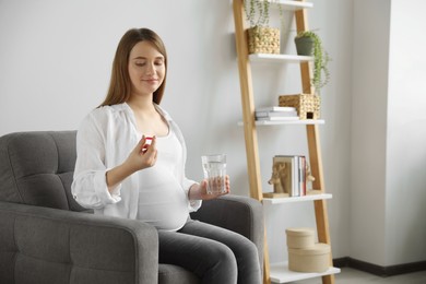 Beautiful pregnant woman holding pill and glass with water at home