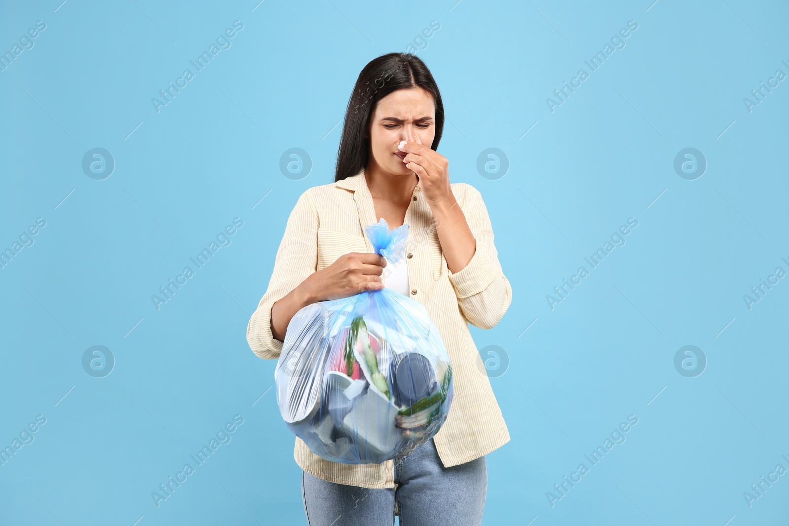 Photo of Woman holding full garbage bag on light blue background