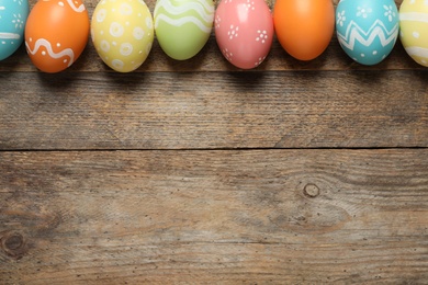 Photo of Flat lay composition of painted Easter eggs on wooden background, space for text