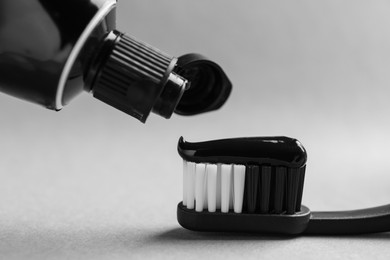 Photo of Applying charcoal toothpaste on brush against light grey background, closeup