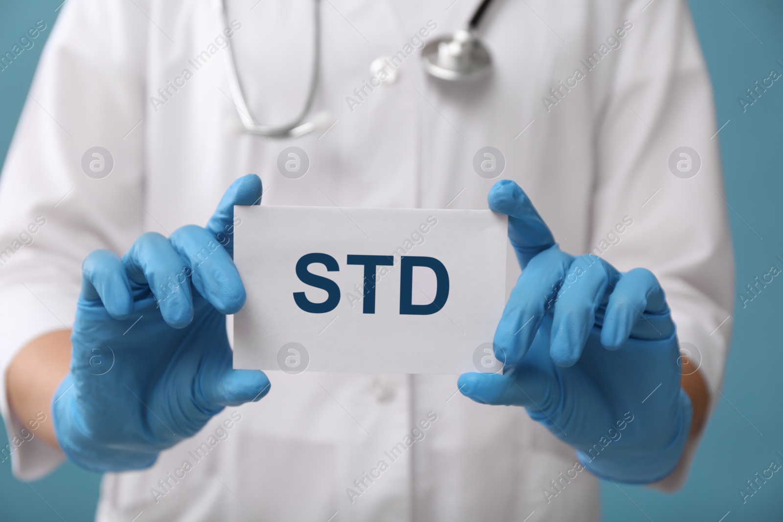 Photo of Doctor holding sheet of paper with abbreviation STD on light blue background, closeup