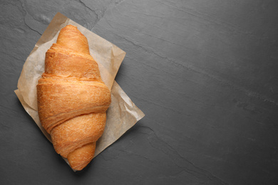 Photo of Tasty fresh croissant on black table, top view. Space for text