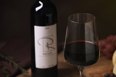 Photo of Glass of red wine with bottle on table, closeup