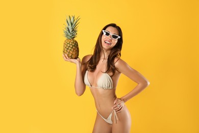 Beautiful woman in stylish bikini and pineapple on yellow background