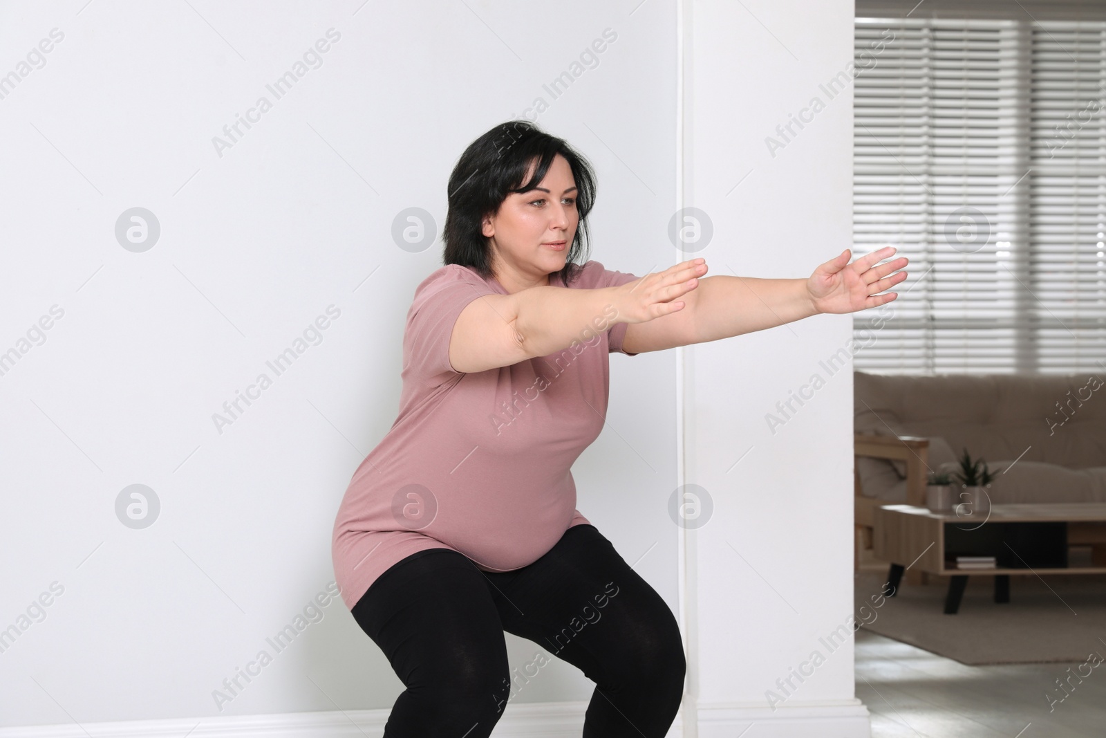 Photo of Overweight mature woman squatting near wall at home