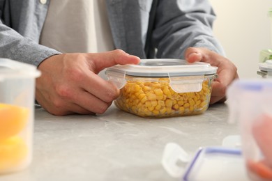 Photo of Man closing glass container with lid at light grey marble table in kitchen, closeup. Food storage