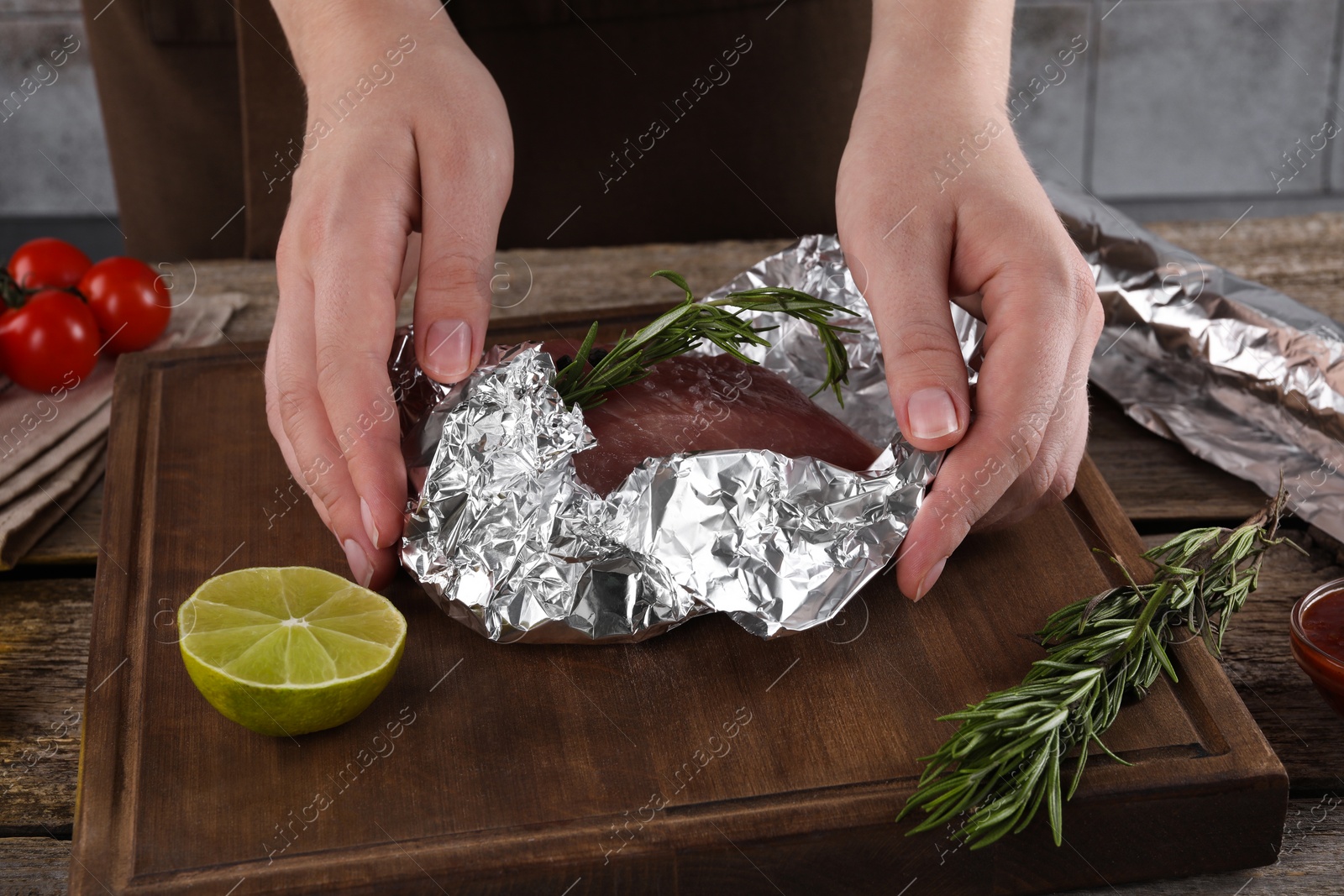 Photo of Woman wrapping meat in aluminum foil at wooden table, closeup