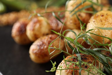 Photo of Delicious grilled potatoes with tarragon on black table, closeup