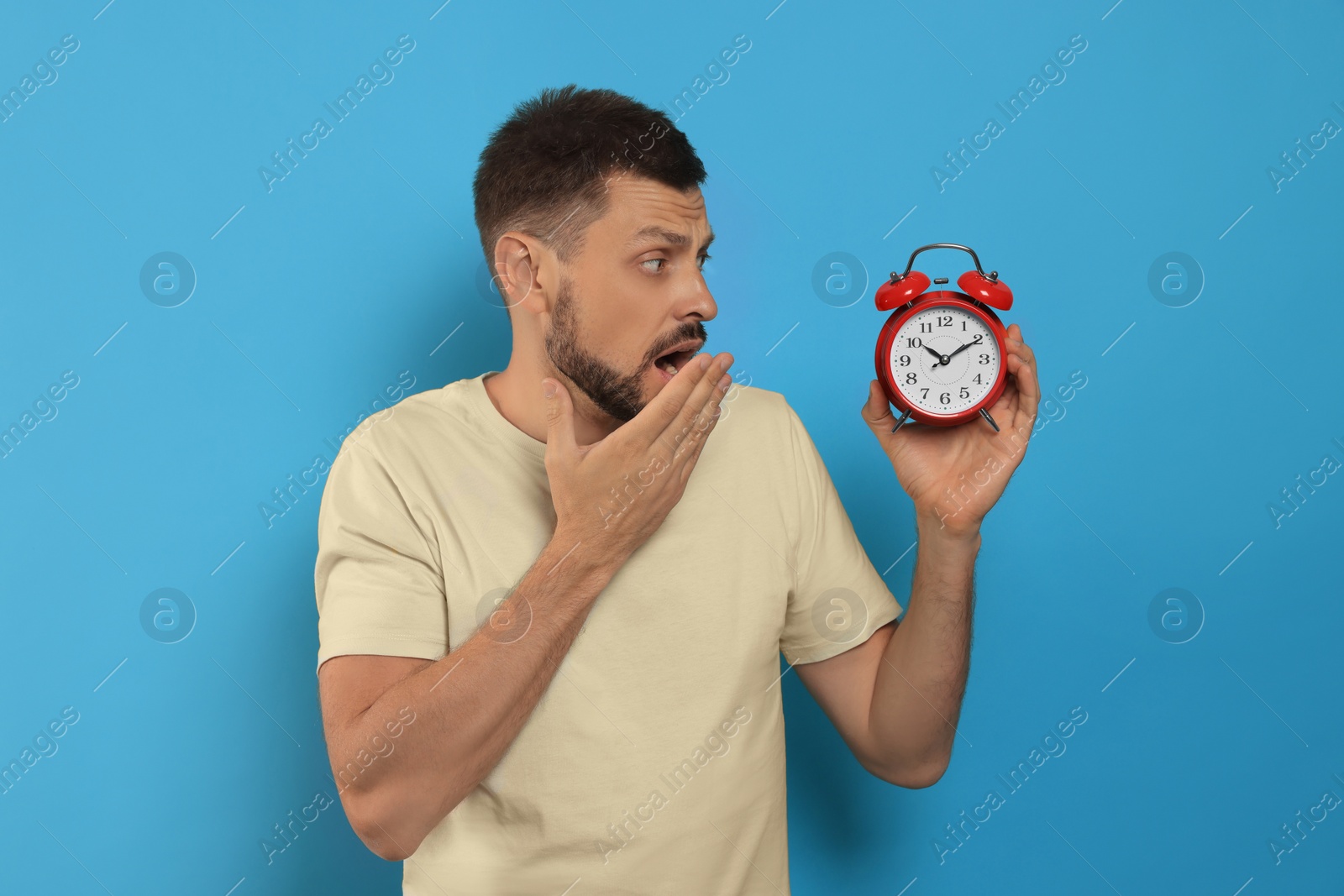 Photo of Emotional man with alarm clock on light blue background. Being late concept