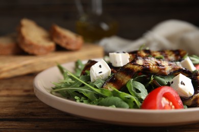 Photo of Delicious salad with roasted eggplant, feta cheese and arugula served on wooden table, closeup
