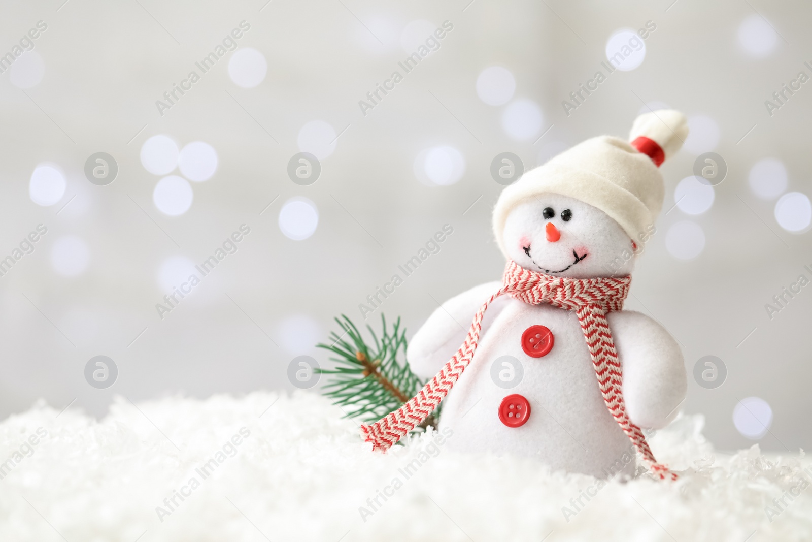 Photo of Snowman toy and branch of fir tree on snow against blurred festive lights, space for text. Christmas decoration
