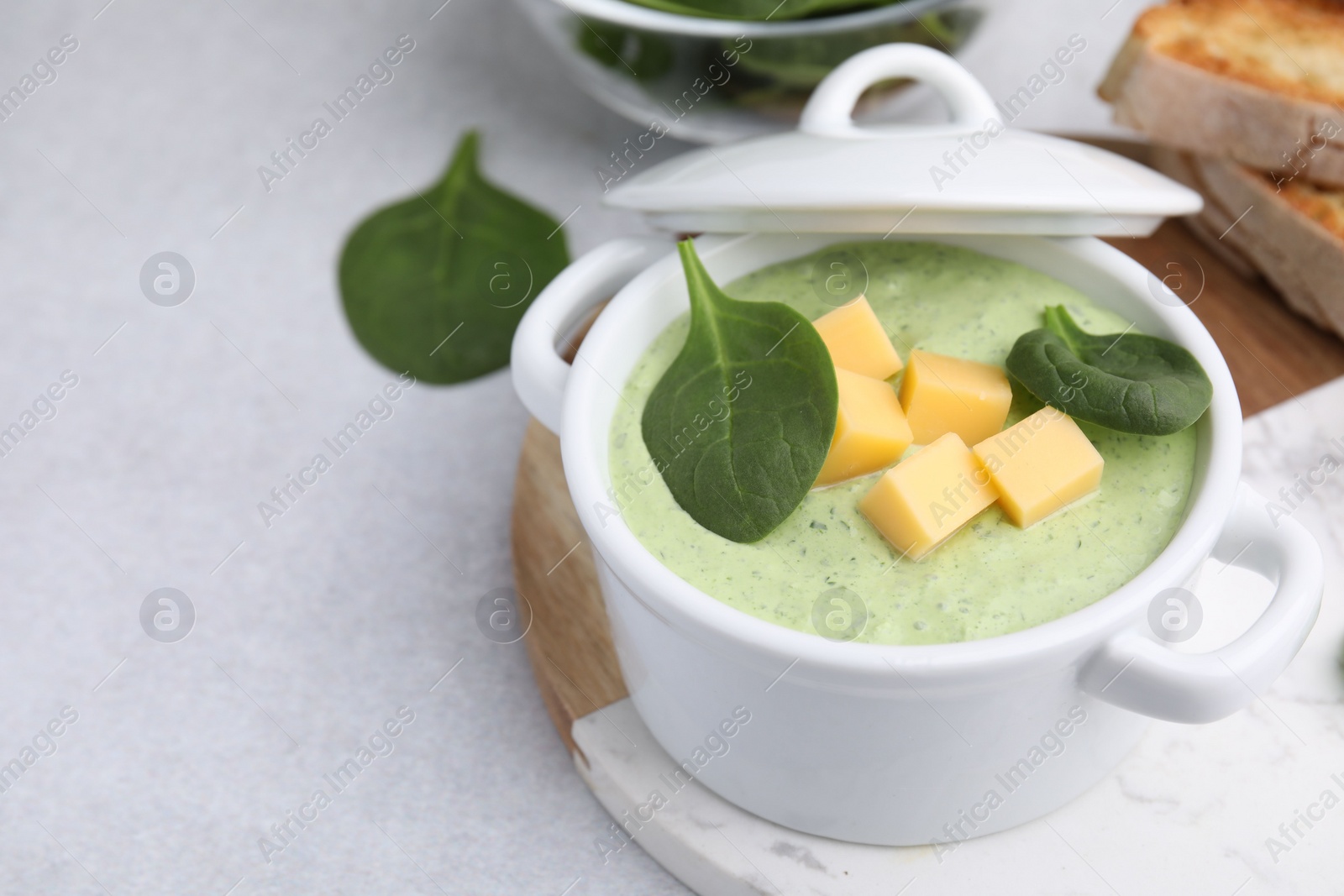 Photo of Delicious spinach cream soup with cheese in bowl on light grey table. Space for text