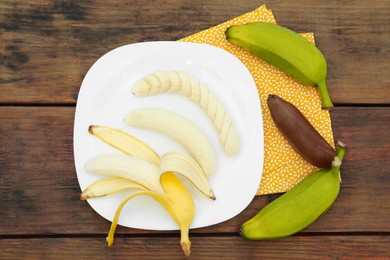 Whole and cut bananas on wooden table, flat lay