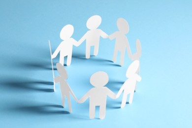 Photo of Teamwork concept. Paper figures of people holding hands on light blue background