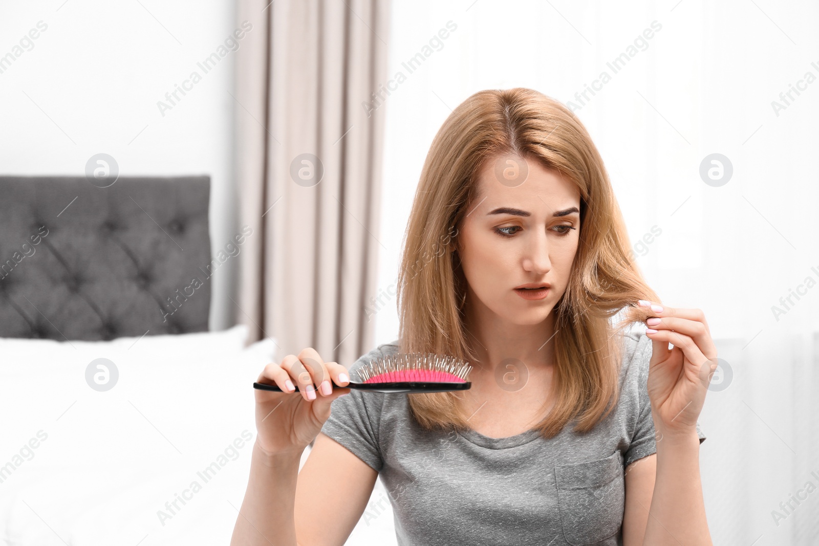 Photo of Attractive young woman brushing hair in bedroom