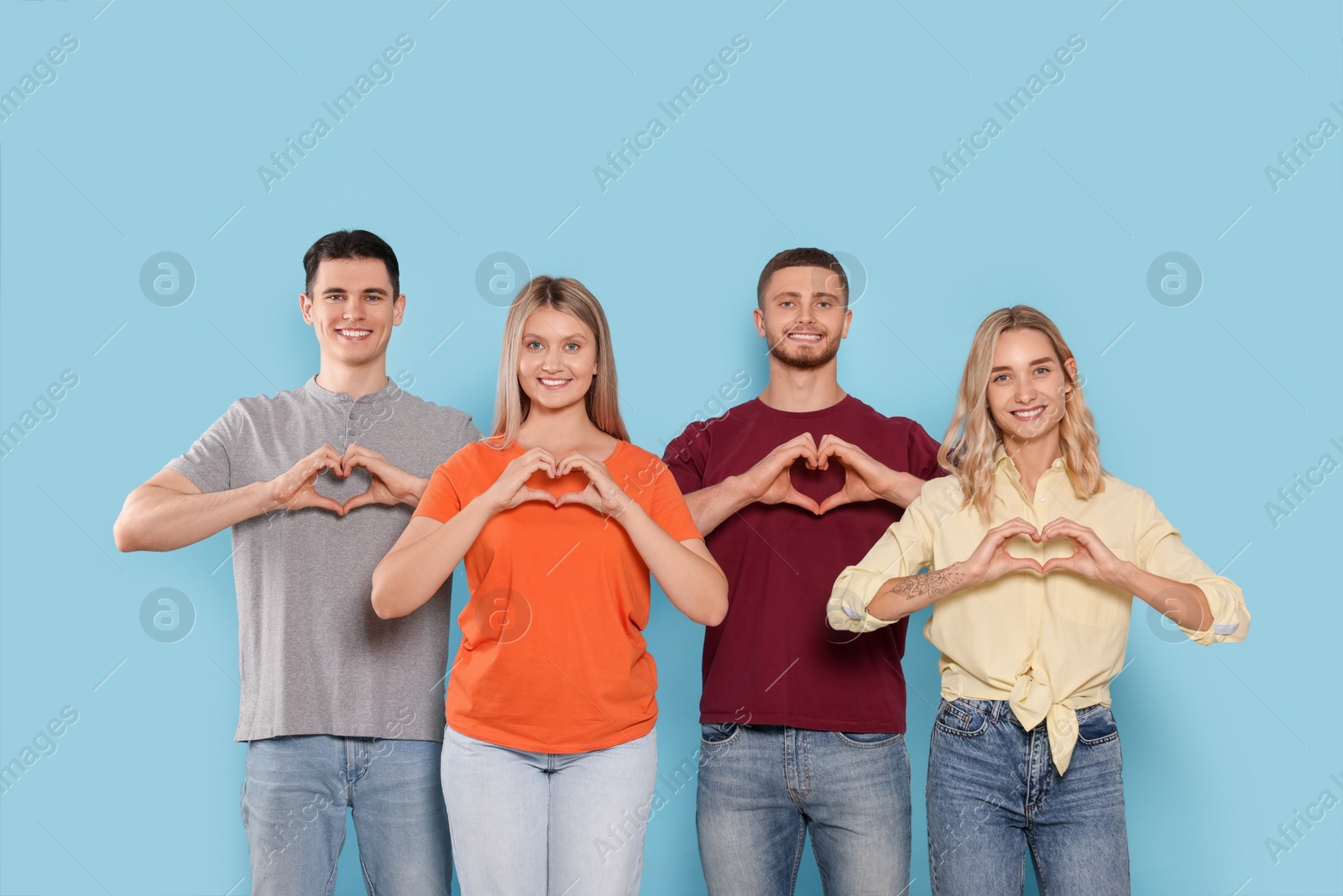 Photo of Happy volunteers making hearts with their hands on light blue background