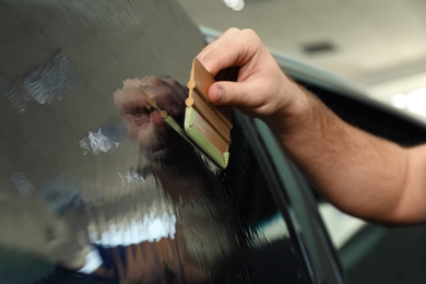 Worker tinting car window with foil in workshop, closeup
