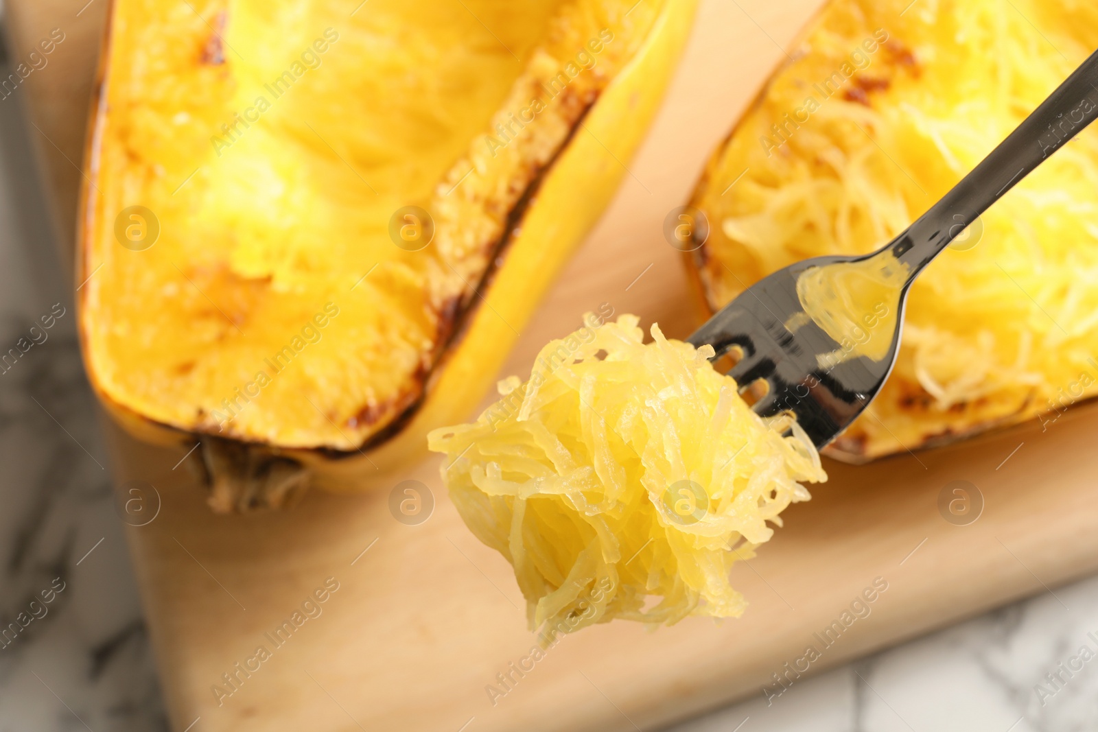 Photo of Fork with flesh of cooked spaghetti squash on blurred background, closeup