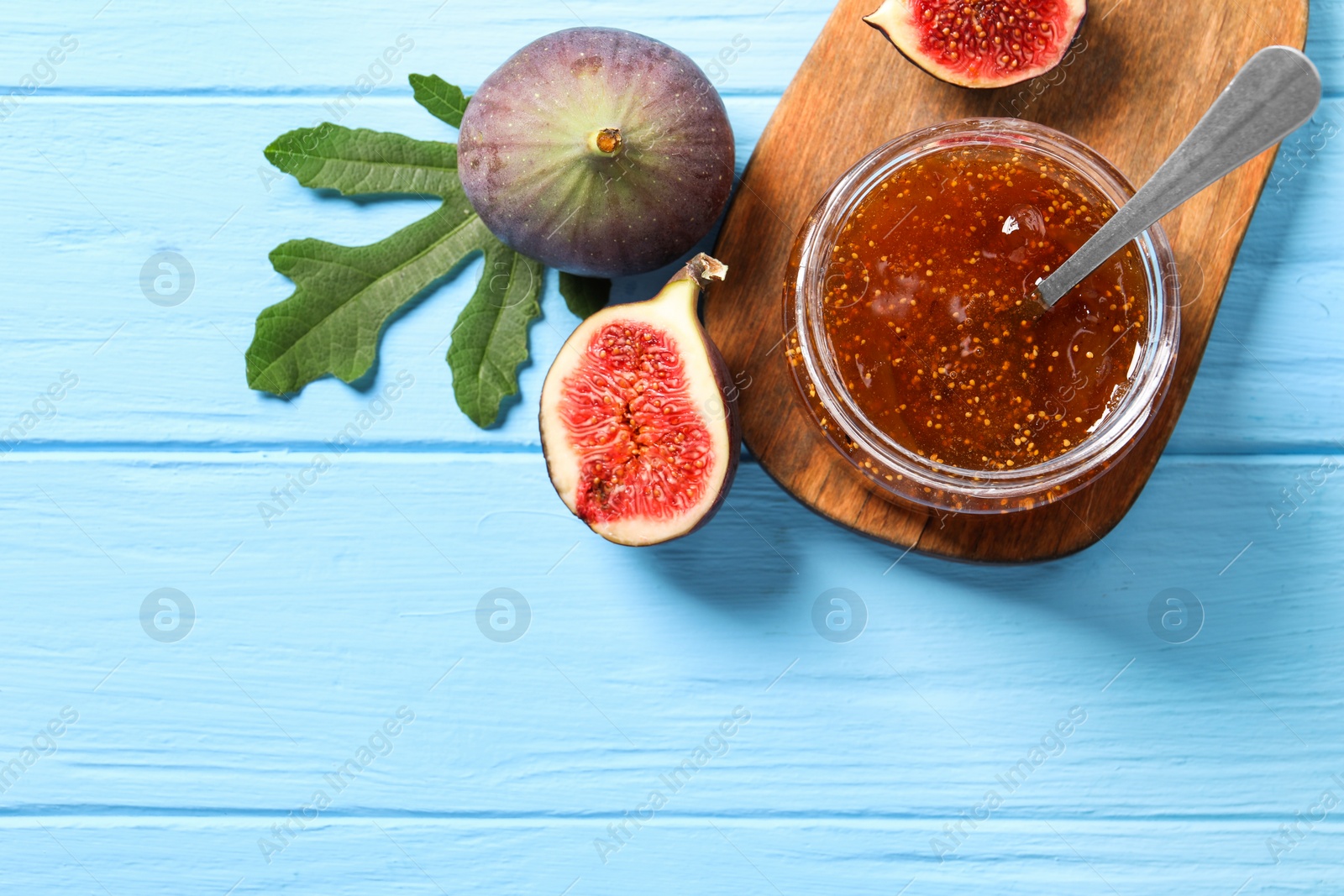 Photo of Jar of tasty sweet jam and fresh figs on light blue wooden table, flat lay. Space for text