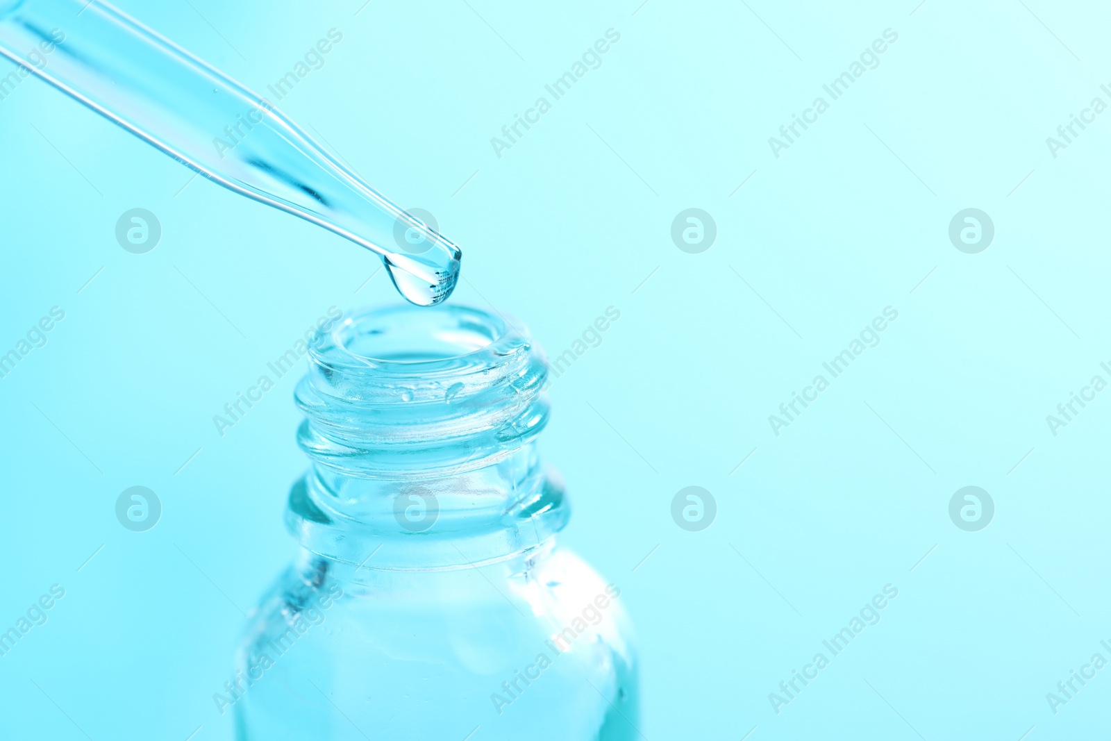 Photo of Dripping liquid from pipette into glass bottle on light blue background, closeup. Space for text