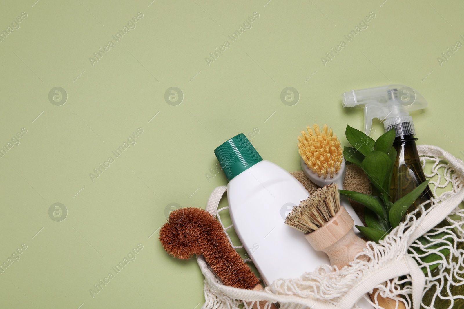 Photo of Different cleaning supplies in string bag on green background, space for text