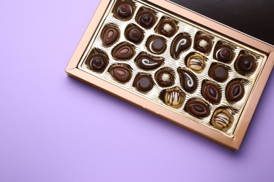 Photo of Box of delicious chocolate candies on violet background, top view. Space for text