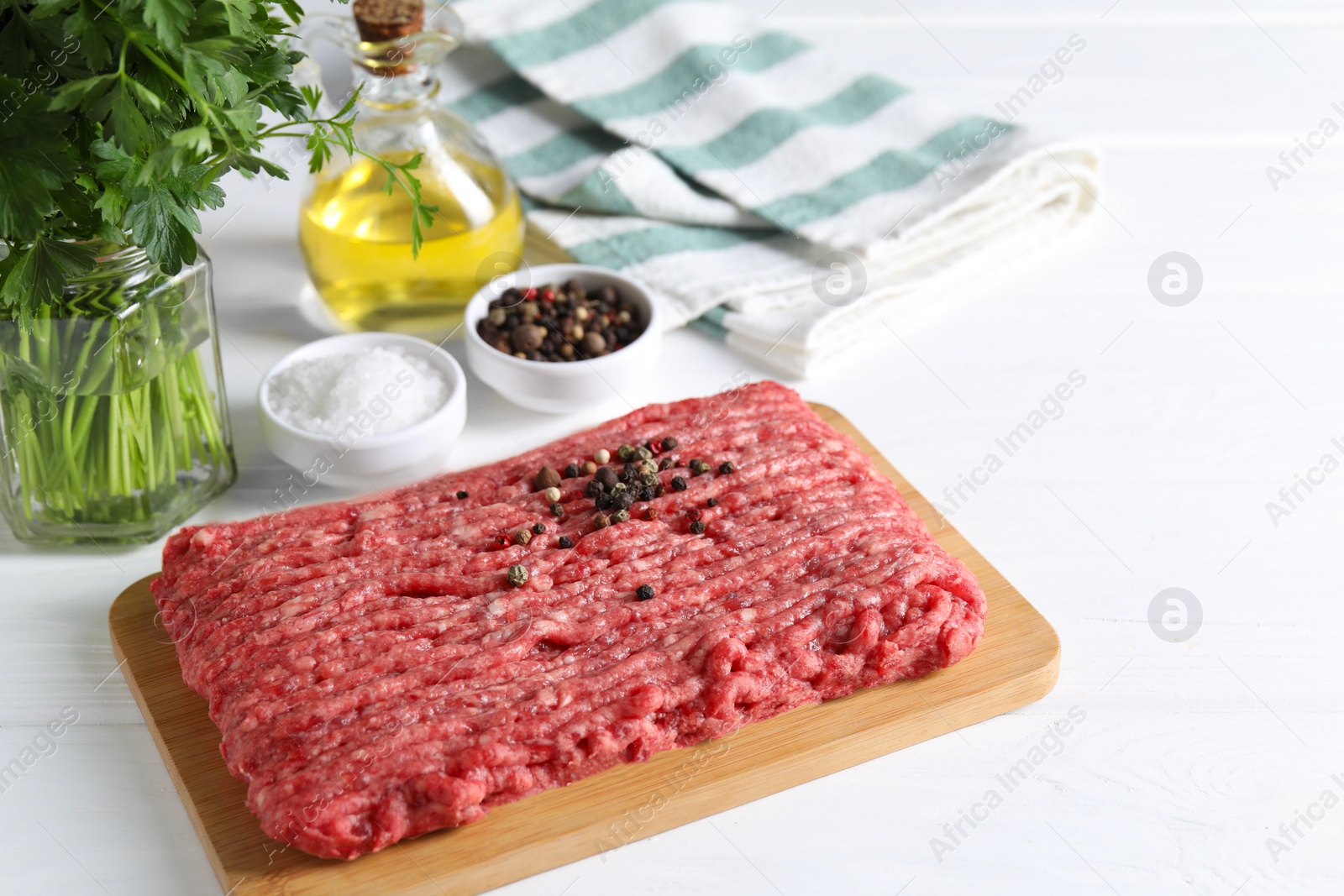 Photo of Raw ground meat, spices, oil and parsley on white wooden table