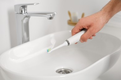 Photo of Man holding electric toothbrush above sink in bathroom, closeup