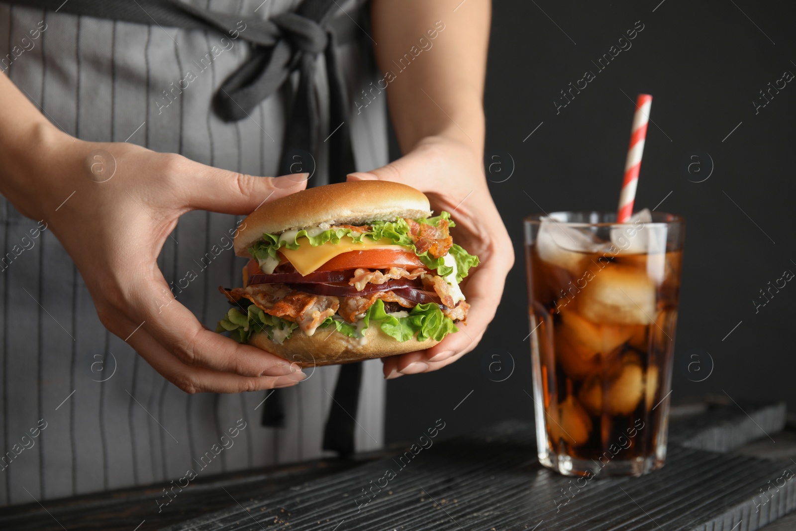 Photo of Woman holding tasty burger with bacon at table, closeup