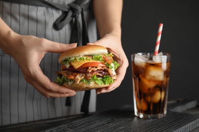 Woman holding tasty burger with bacon at table, closeup