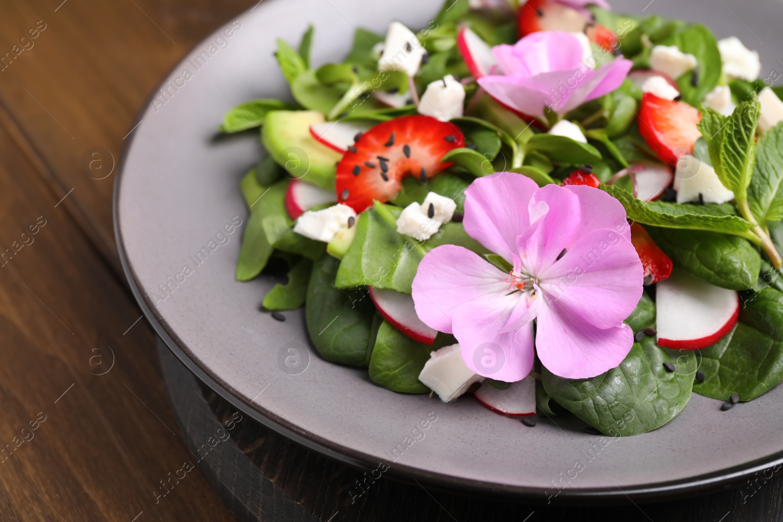 Photo of Fresh spring salad with flowers on wooden table, closeup