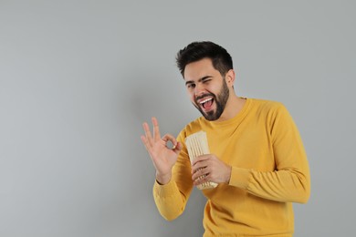 Happy young man with tasty shawarma showing okay gesture on grey background. Space for text