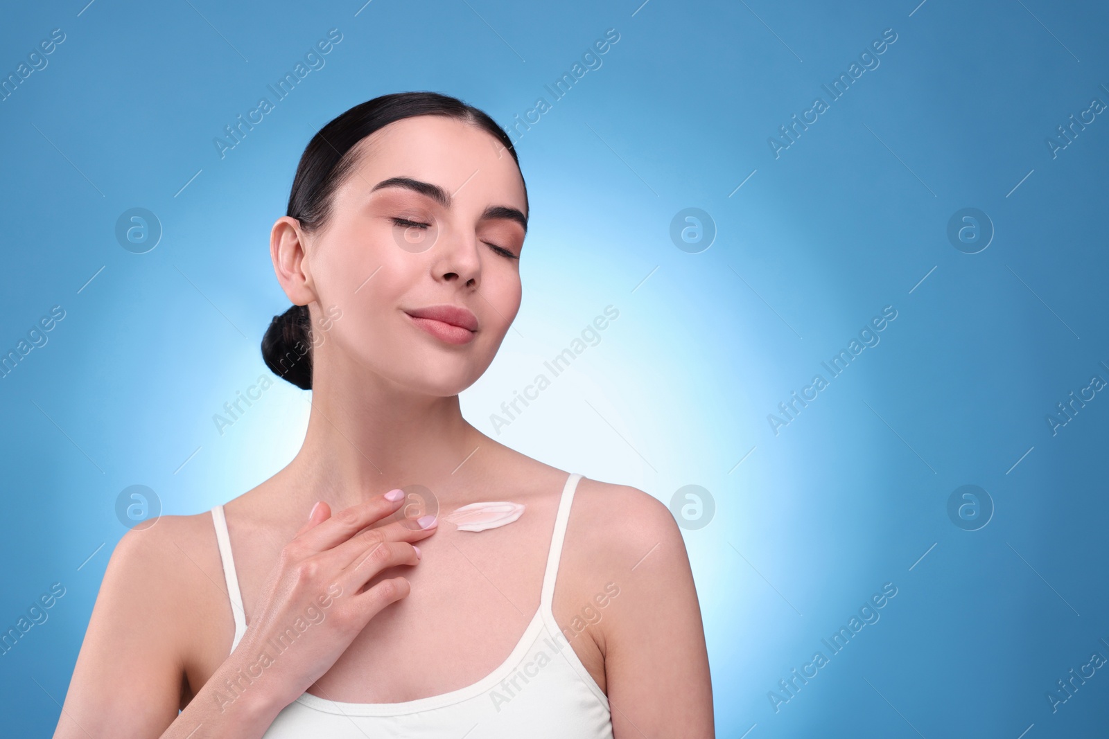 Photo of Beautiful woman with smear of body cream on her collarbone against light blue background, space for text