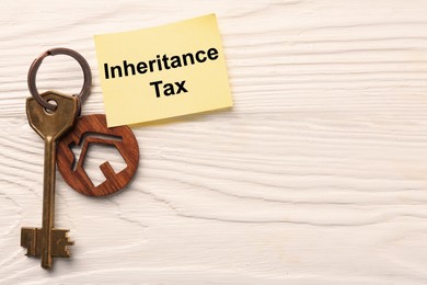 Photo of Inheritance Tax. Paper note and key with key chain in shape of house on white wooden table, flat lay. Space for text