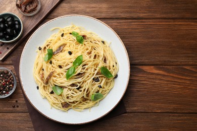 Photo of Delicious pasta with anchovies, olives and basil on wooden table, flat lay. Space for text