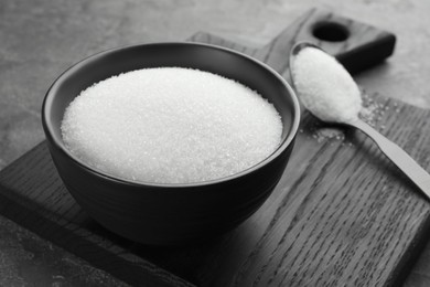 Photo of Granulated sugar in bowl on grey textured table, closeup